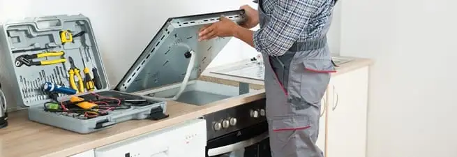 Cooktop repair technician lifting a built-in stovetop for service in Baltimore, MD
