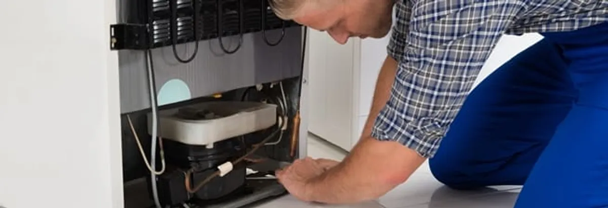 Refrigerator repair technician servicing the compressor and condenser area in Baltimore, MD