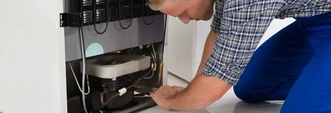 Refrigerator repair technician servicing the compressor and condenser area in Baltimore, MD