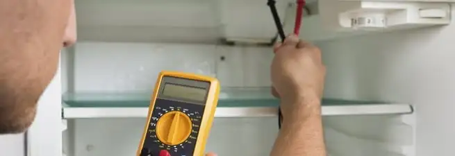 Refrigerator repair technician testing electrical components with a multimeter in Baltimore, MD
