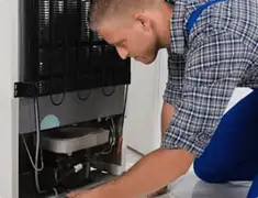 Refrigerator repair technician servicing the compressor and condenser area in Baltimore, MD
